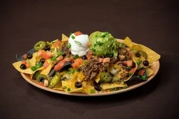 Large plate of nachos with melted cheese, shredded meat, guacamole, sour cream.