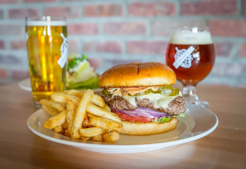 Well-stacked cheeseburger, golden fries, and two beers in a restaurant.