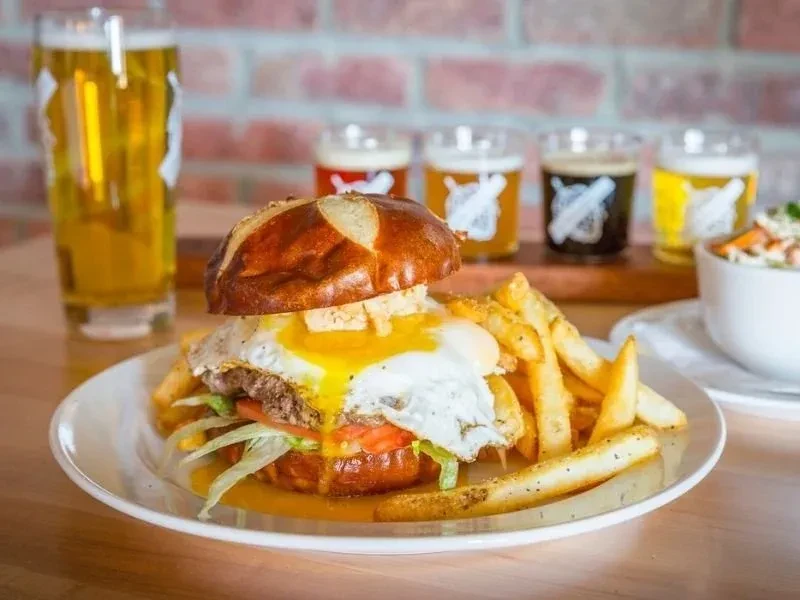Pretzel bun burger with runny egg, fries, and beer flight.