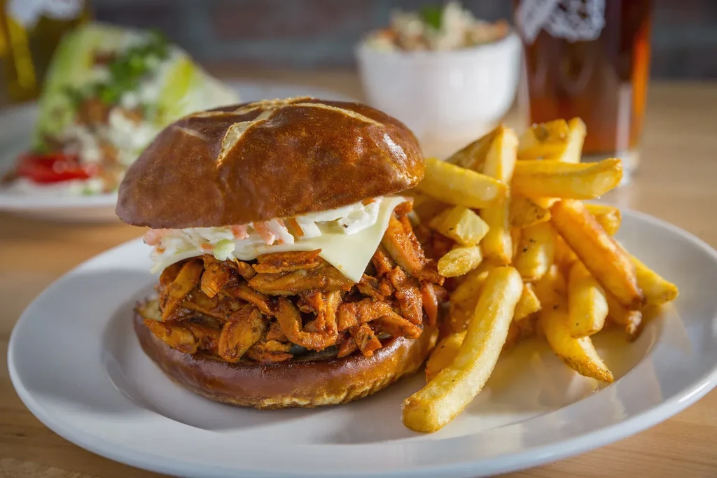 Pulled meat sandwich with coleslaw on a pretzel bun, with fries.
