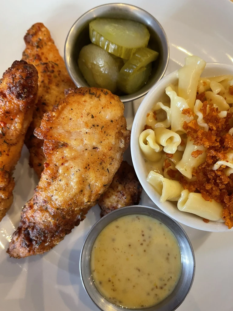 Fried chicken, mac and cheese, pickles, and honey mustard on a white plate.