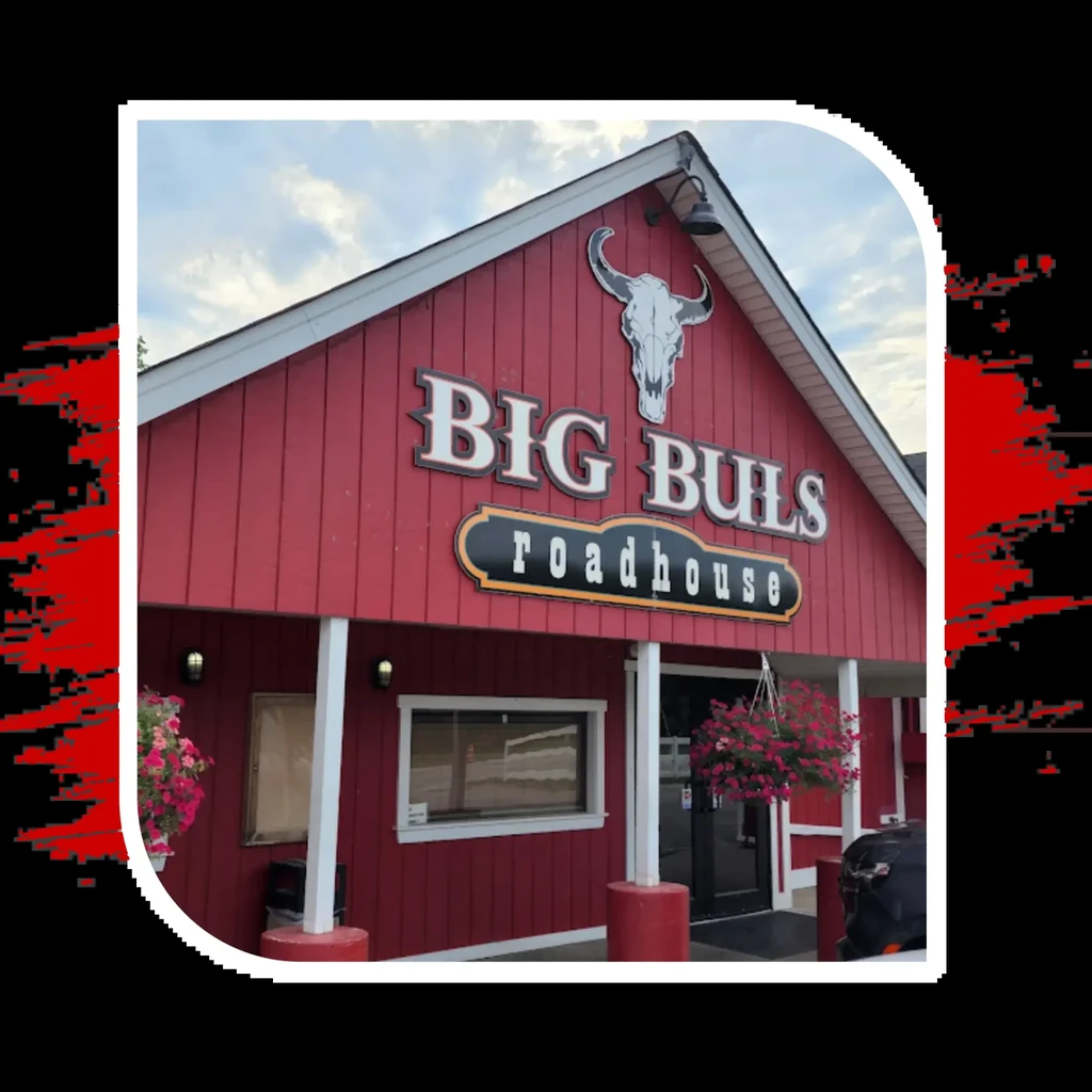 Exterior of BIG BULS roadhouse, red siding, bull skull sign, pink flowers.