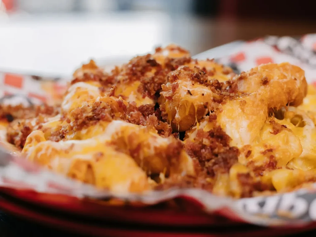 Tater tots with melted cheese and crumbled bacon in a basket.