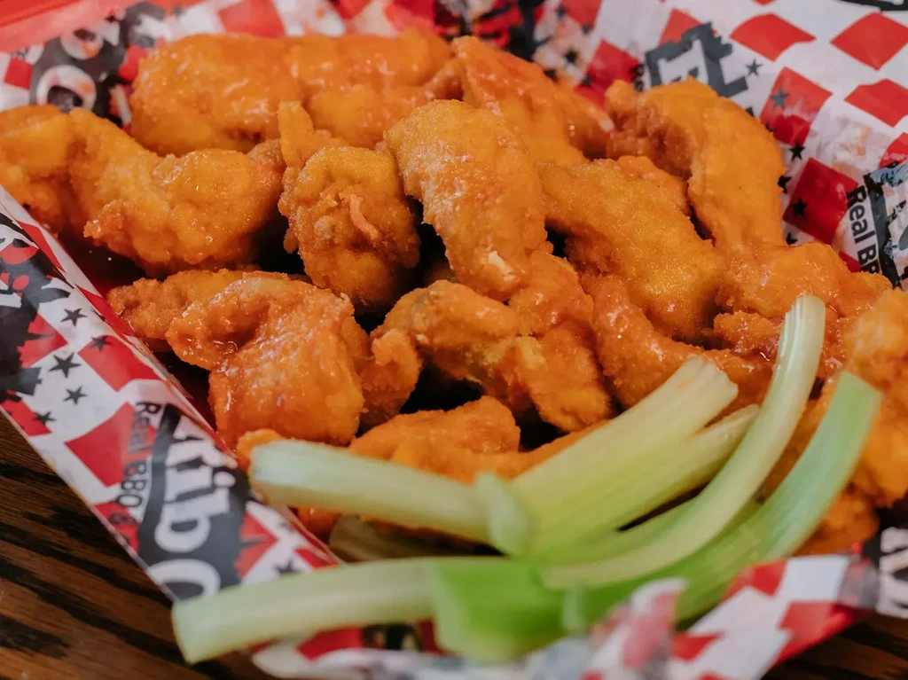 Orange-sauced chicken wings or shrimp with celery in a patterned basket.
