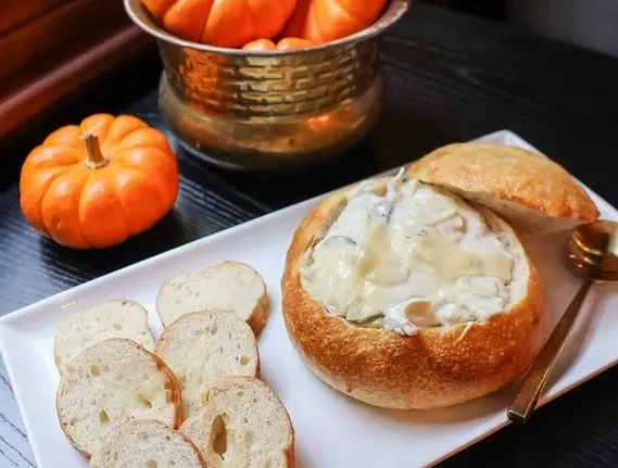 Rustic bread bowl of creamy soup, baguette, and fall decorations.