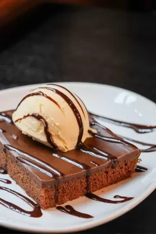 Chocolate brownie with vanilla ice cream and chocolate drizzle on a plate.