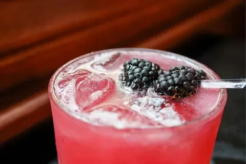 A pink cocktail with ice cubes, garnished with two blackberries.