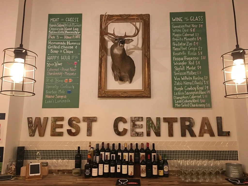 Bar counter with wine, menus, deer head, and 'WEST CENTRAL' sign.