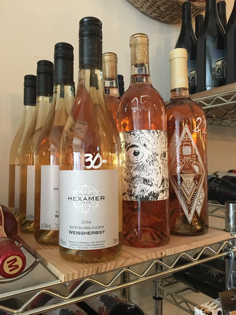 Close-up of white and rosé wine bottles with various labels on shelves.