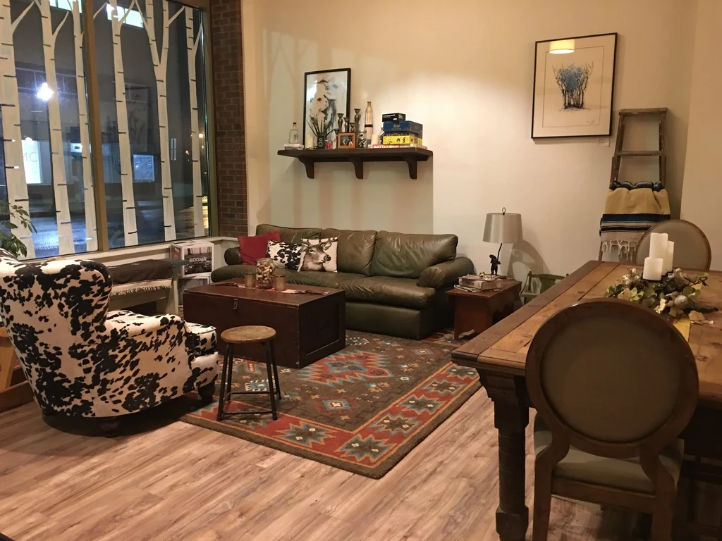 Cozy rustic lounge and dining area with cow-print chair and green sofa.