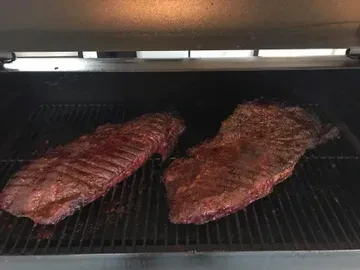 Two large briskets with dark bark smoking on a grill grate.