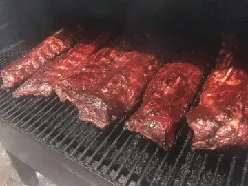 Glossy racks of dark red ribs cooking inside a smoker.