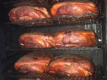 Six large smoked meats with reddish-brown bark on racks.