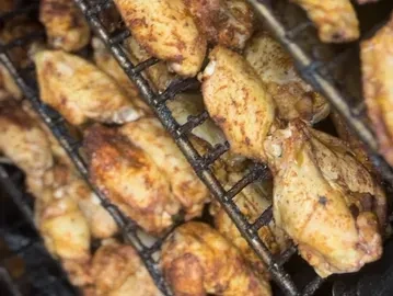 Seasoned golden-brown chicken wings on a dark, multi-tiered cooking rack.