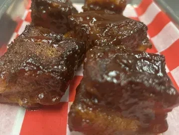 Close-up of caramelized barbecued meat in dark sauce on checkered paper.