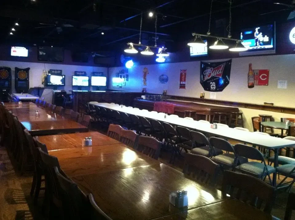Dimly lit, empty sports bar with wooden tables, a bar, TVs, dartboards.