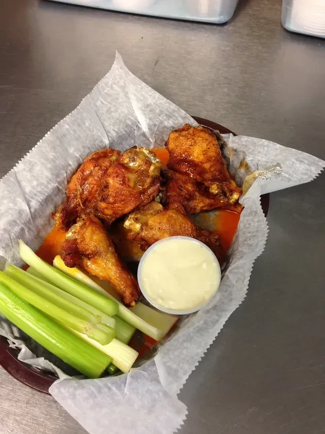 Basket of buffalo chicken wings, celery sticks, and dipping sauce.
