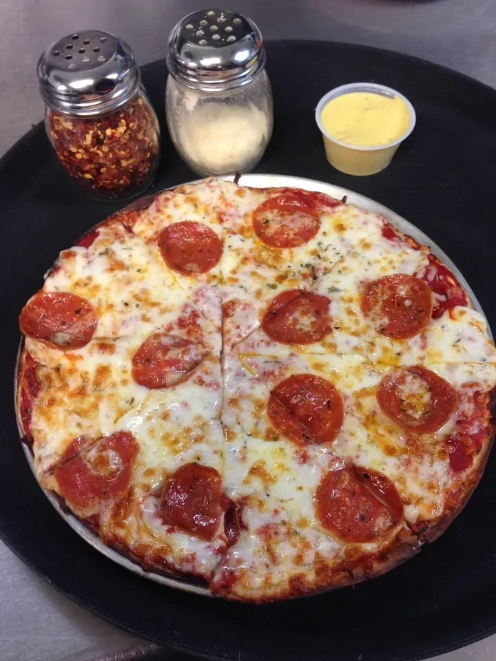 Freshly baked pepperoni pizza, sliced, with red pepper, Parmesan, and dipping sauce.