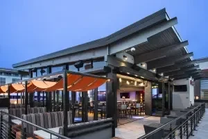 Contemporary restaurant patio with orange canopies and lit bar at dusk.