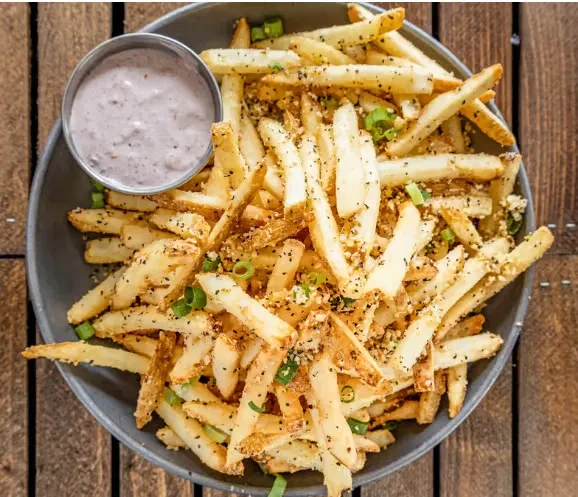 Crispy seasoned fries, purple speckled dip in a bowl on wood.