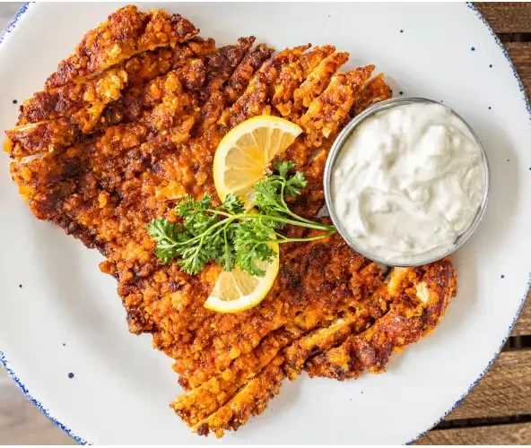 Crispy breaded cutlet, lemon, parsley, dipping sauce on a rustic wooden table.