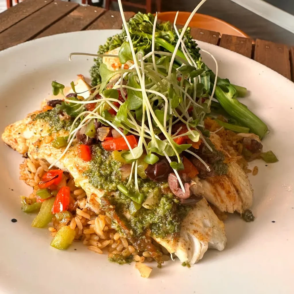 Plated fish fillets with green sauce, sprouts, brown rice, and broccolini.