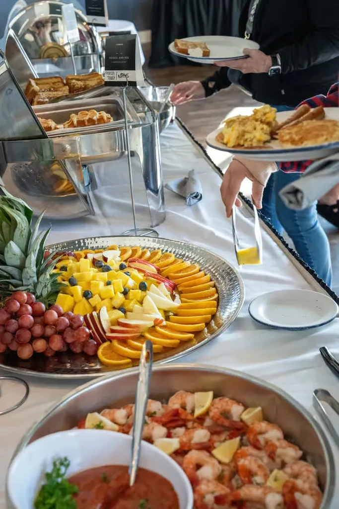 People serving themselves from a breakfast buffet with fruit and hot dishes.