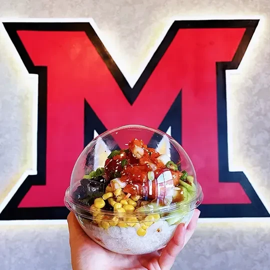 Hand holds colorful poke bowl before a red 'M' logo.