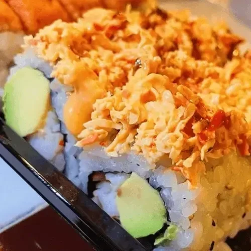 A generously topped sushi roll with orange crab topping and avocado.