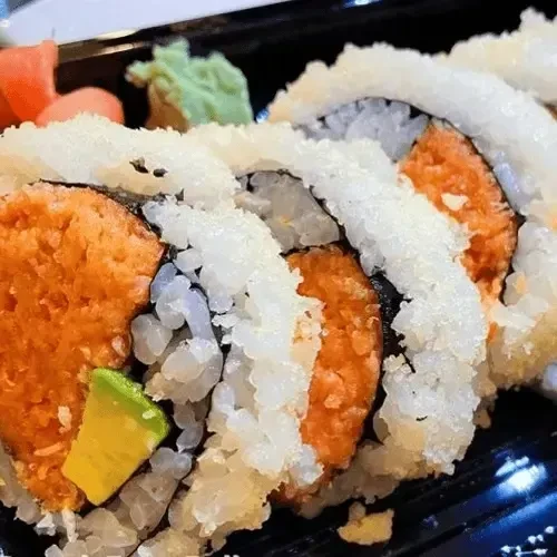 Orange-filled sushi rolls with avocado and tempura flakes in a container.