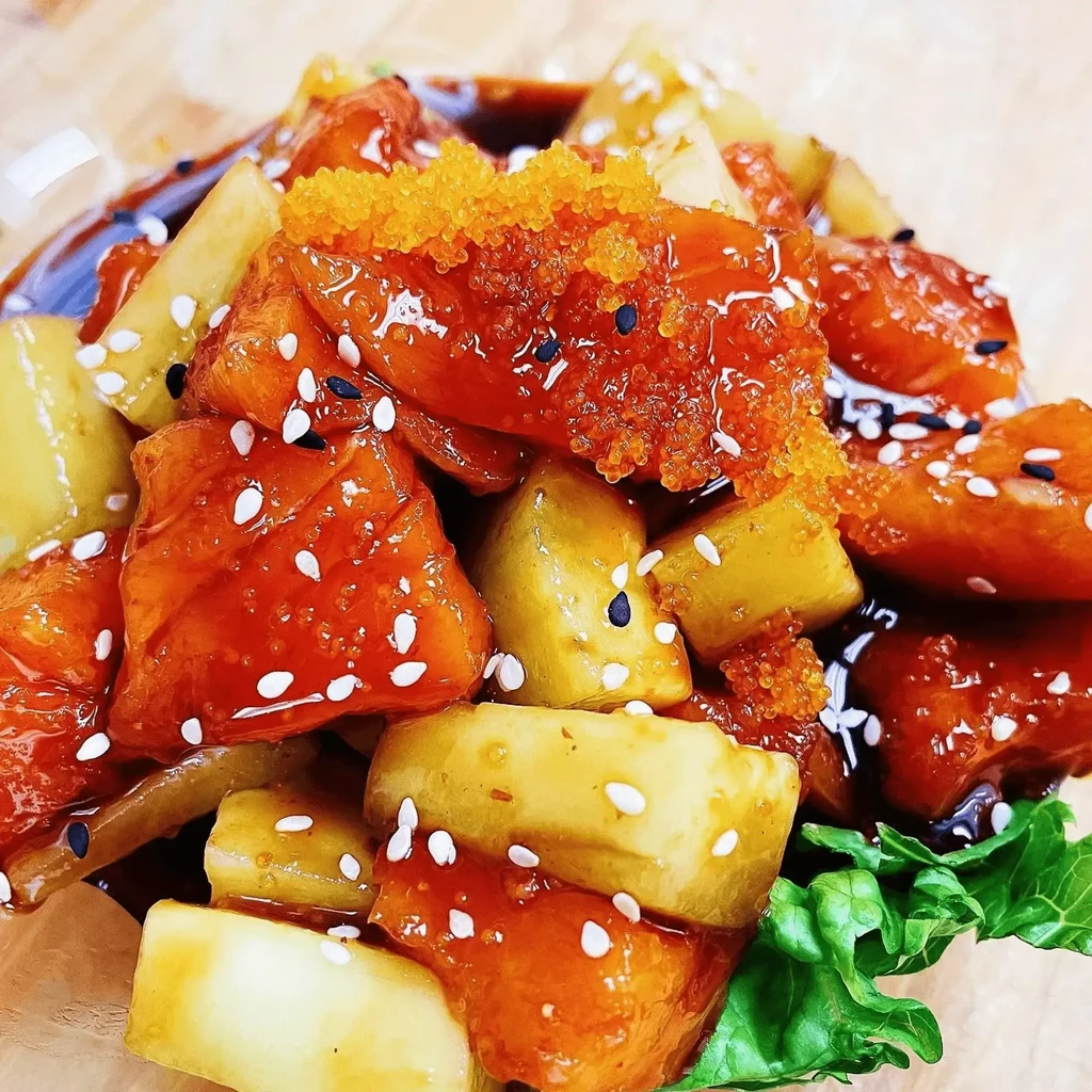 Glazed reddish-orange dish with yellow chunks, tobiko, sesame, and green garnish.