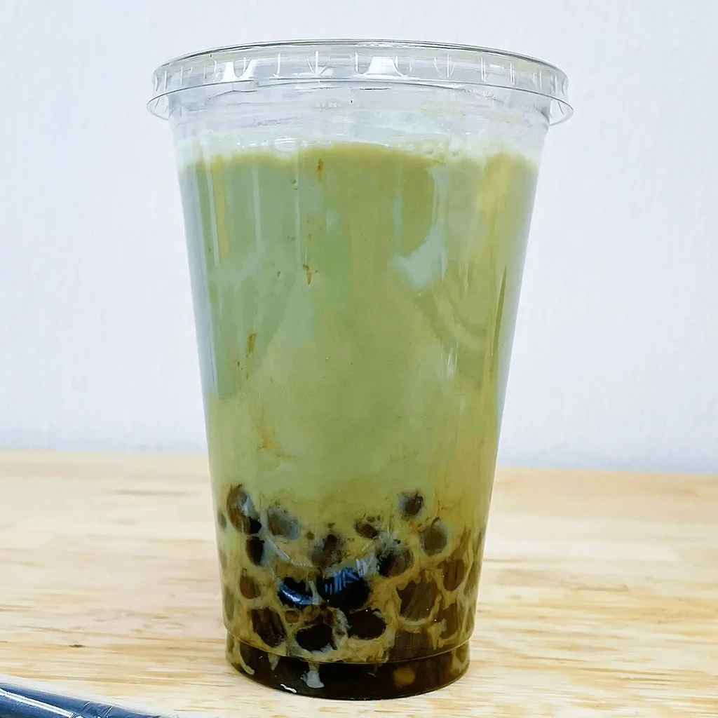 Clear plastic cup with layered green drink and brown tapioca pearls.