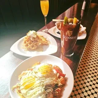 Breakfast dishes, Bloody Mary, and mimosa on a dark bar counter.