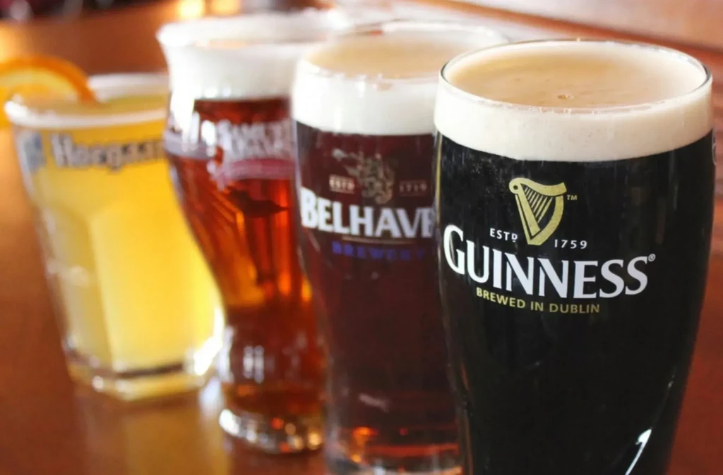 Four distinct glasses of beer, including Guinness and Belhaven, on a bar.