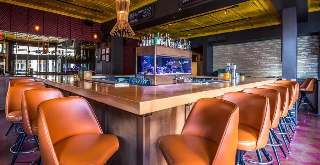 Modern bar with wooden counter, orange stools, integrated fish tank.