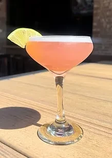 Pinkish-orange cocktail with foam and citrus wedge on wood.