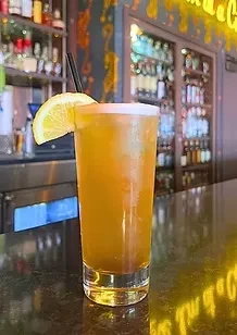 Frothy amber drink with lemon and straw on a bar.