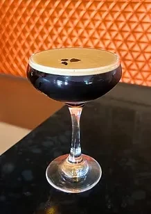 Espresso martini in coupe glass, foam, and coffee beans.