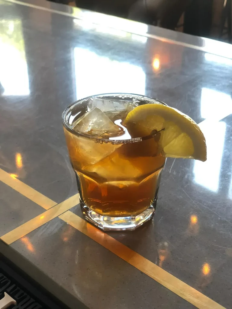 Amber cocktail with lemon on grey counter featuring gold stripes.