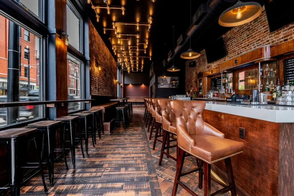 Modern industrial-chic bar interior with exposed brick, copper pipes, and leather stools.