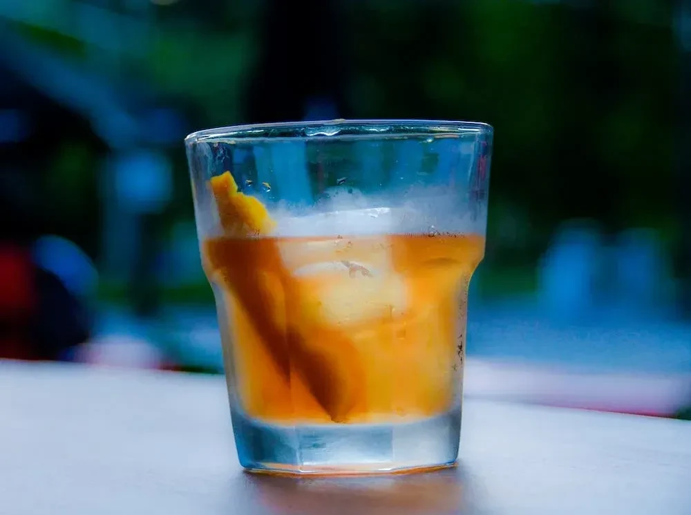 Amber cocktail with ice and citrus twist in a faceted glass.