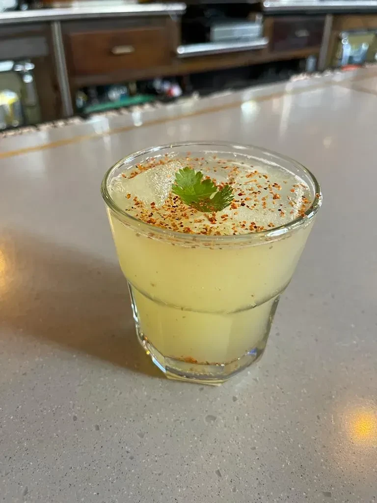 Yellow-green drink in faceted glass with ice, a green leaf, and spice.