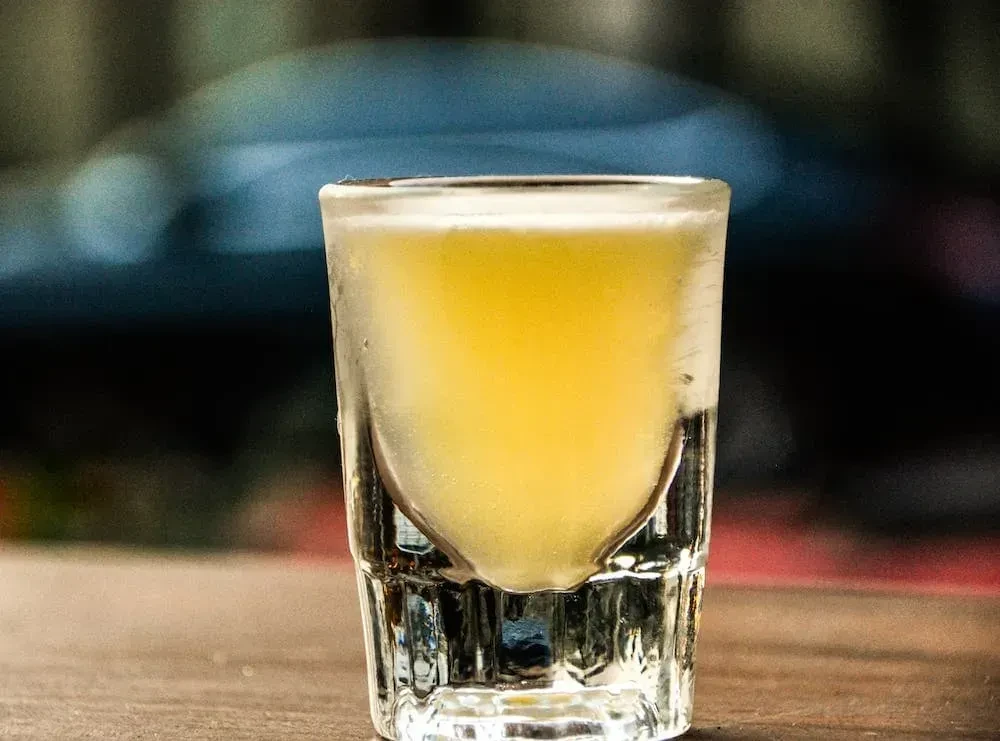 Frosted shot glass with amber liquid on a wooden table.