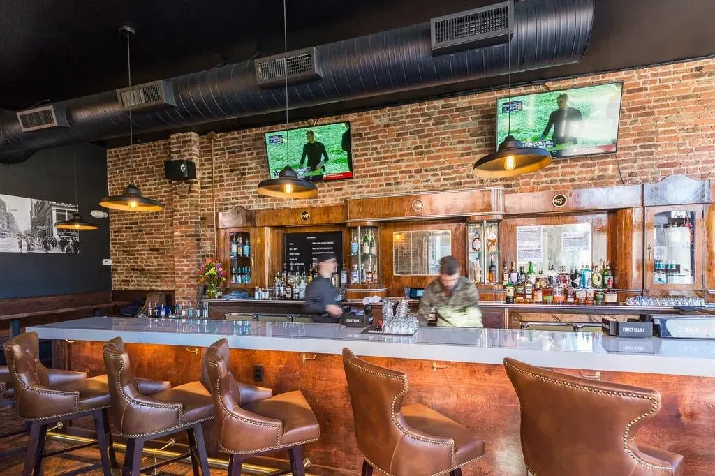 Modern industrial bar with light counter, leather stools, and sports TVs.