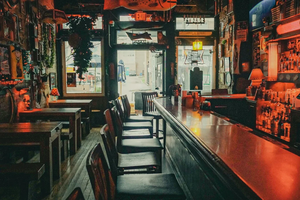 Rustic bar interior featuring dark wood, dim reddish lighting, and decorated walls.
