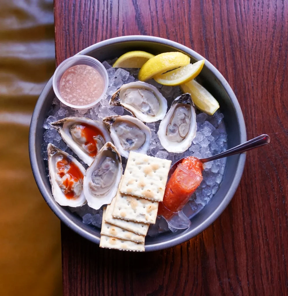 Six raw oysters on ice with lemon, cocktail sauce, and mignonette.