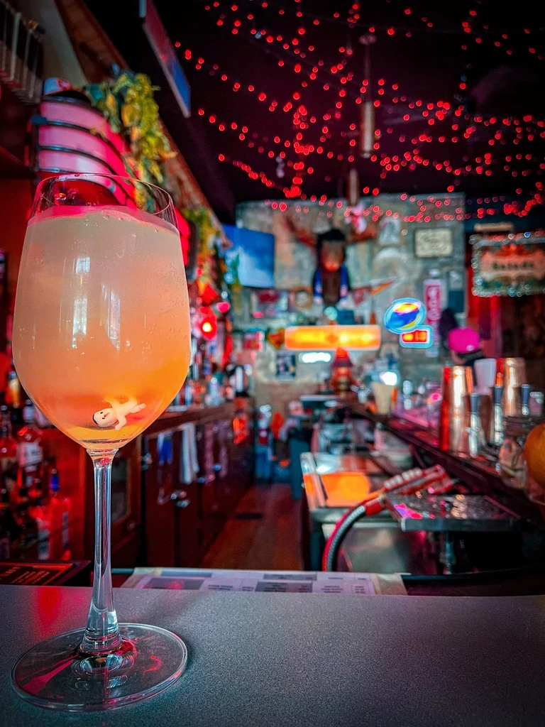 Glass of foamy orange cocktail with a tiny floating figure.