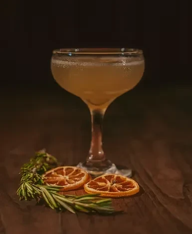 Effervescent amber cocktail in a coupette glass with orange and rosemary.