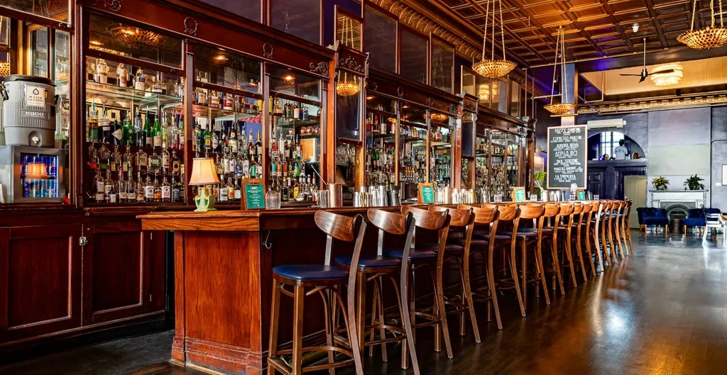 Wide, elegant wooden bar with stools and mirrored liquor display.