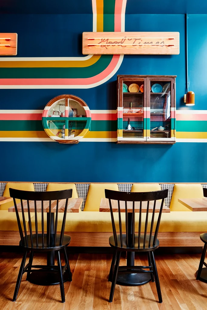 Retro restaurant with colorful striped wall, yellow booth, "Good Times" sign.